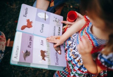 An image of a girl diagnosed with autism reading from a colourful book having pictures and words as a part of her speech and language therapy.